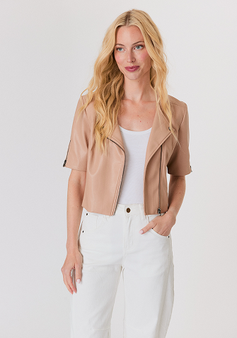 Blonde woman wearing a black and white sweater with a snowflake pattern and blue jeans standing against a light gray background.