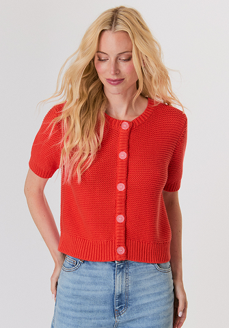 Blonde woman in a navy button-up shirt with embellished collar and light blue jeans against a plain background.