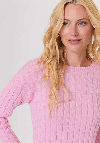 Woman wearing a red sweater with white and red star patterns, paired with white pants, standing against a light background.