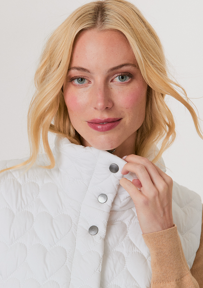 Blonde woman wearing a dark brown cropped cardigan with a satin ribbon tie over a white top and light blue high-waisted jeans.