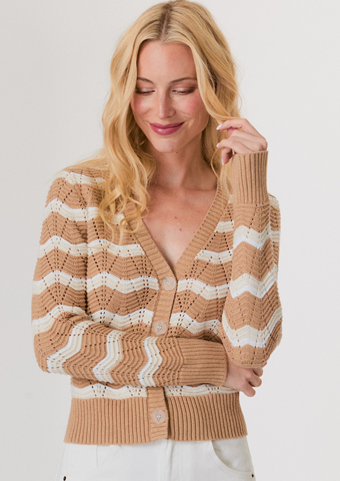 Blonde woman wearing a white button-up shirt with pockets and white pants, posing with hands in pockets against a light background.