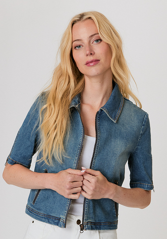 Woman wearing a white long-sleeve top with fluffy cuffs and blue wide-leg jeans, standing against a plain background.