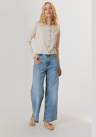 Woman wearing a red sweater with white and red star patterns, paired with white pants, standing against a light background.