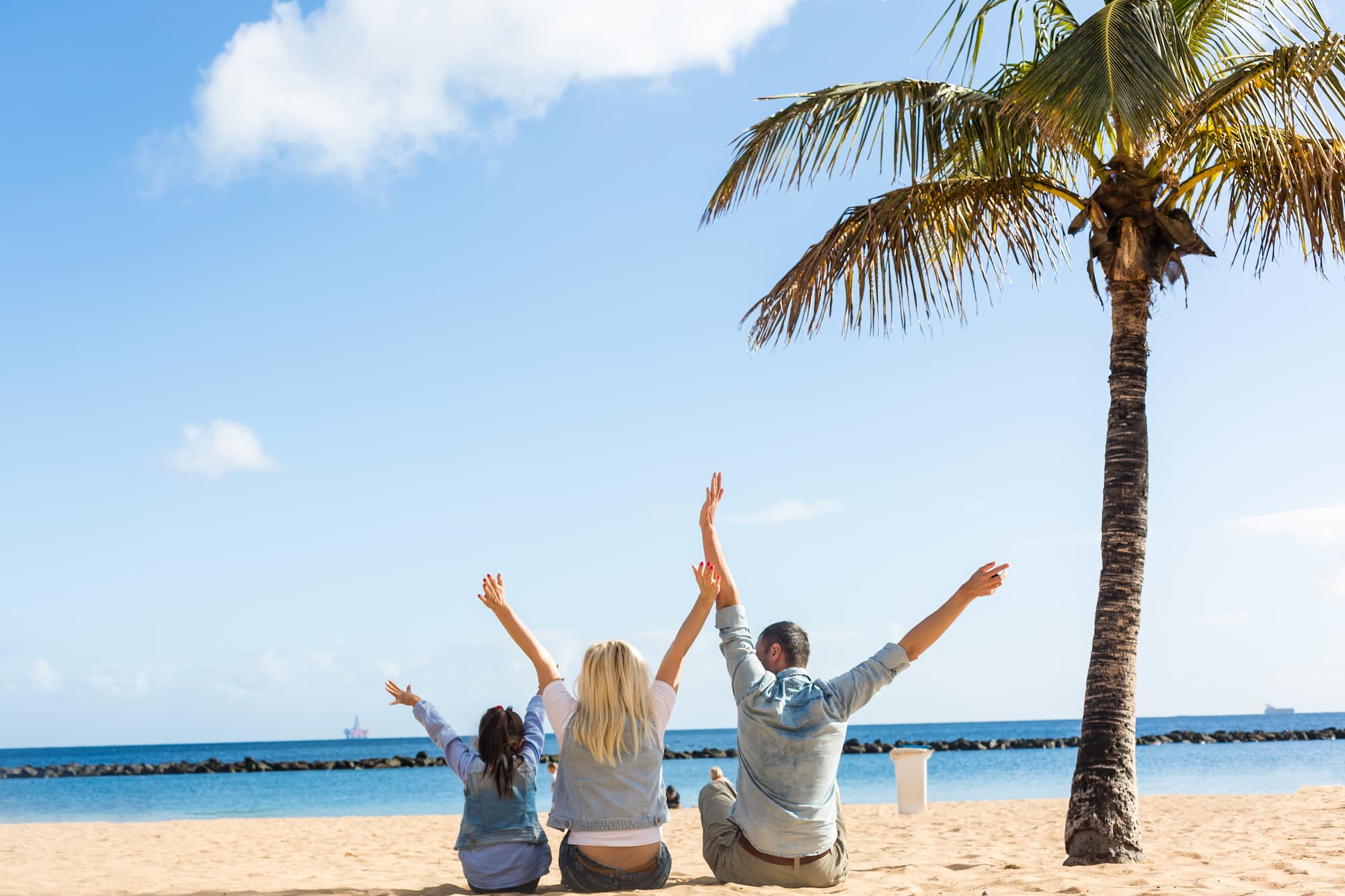 family raising their hands on sunny tropical beach