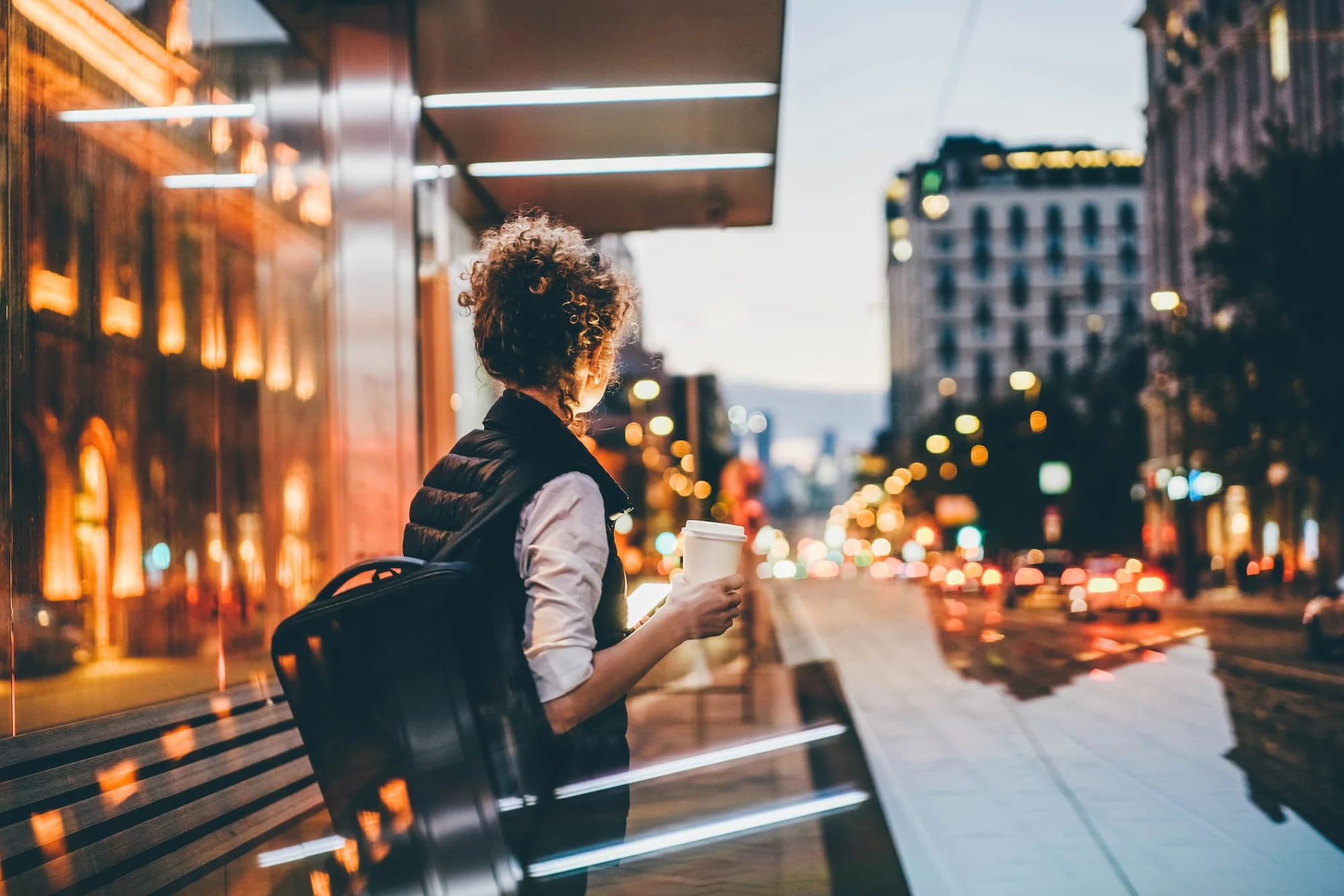 business woman waiting for public transit in lit up city