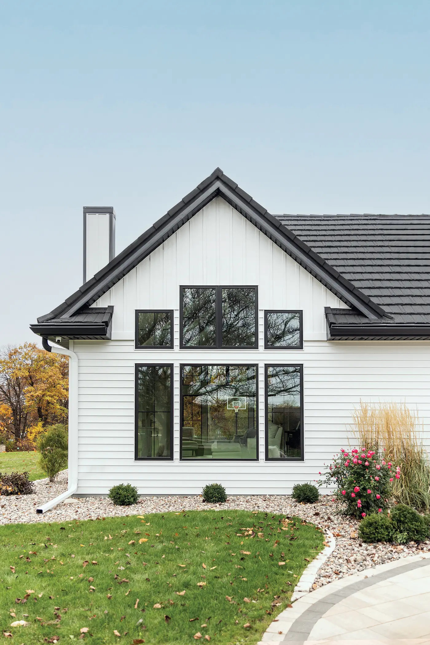 Modern farmhouse exterior featuring large black-framed windows arranged symmetrically on a white façade, highlighting expansive glass that brings in natural light and frames outdoor views.