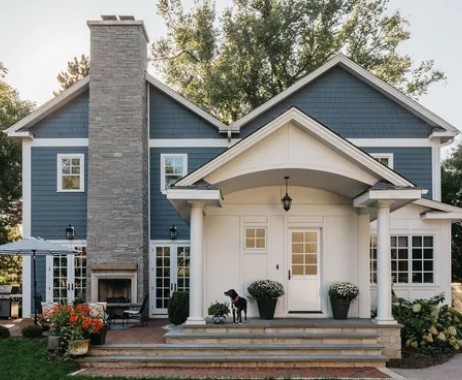 Coastal-style home featuring James Hardie fiber cement siding in blue with white trim, covered front porch, stone chimney, and landscaped entry.