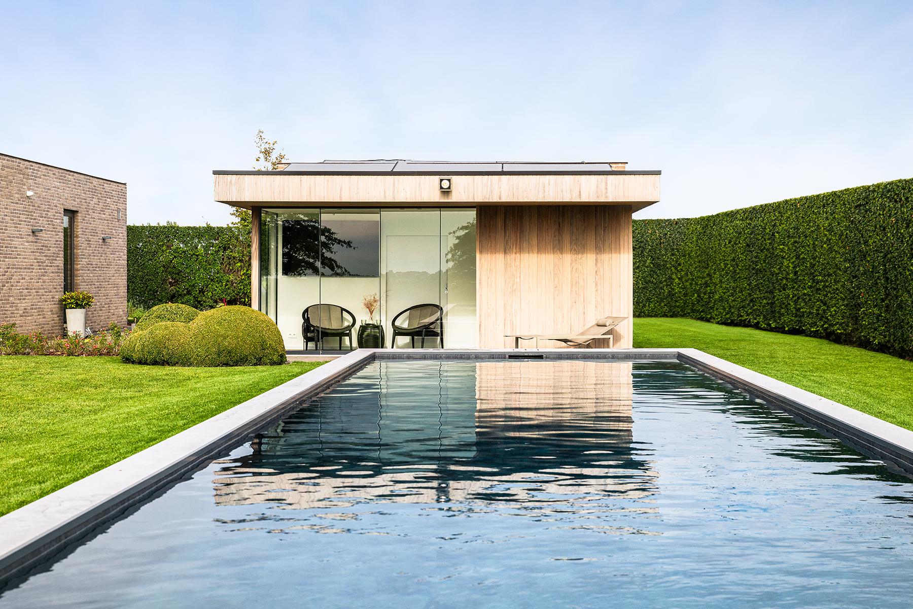 Zwembad afgewerkt met tegels rondom en grasrand in landelijke omgeving, met houten poolhouse