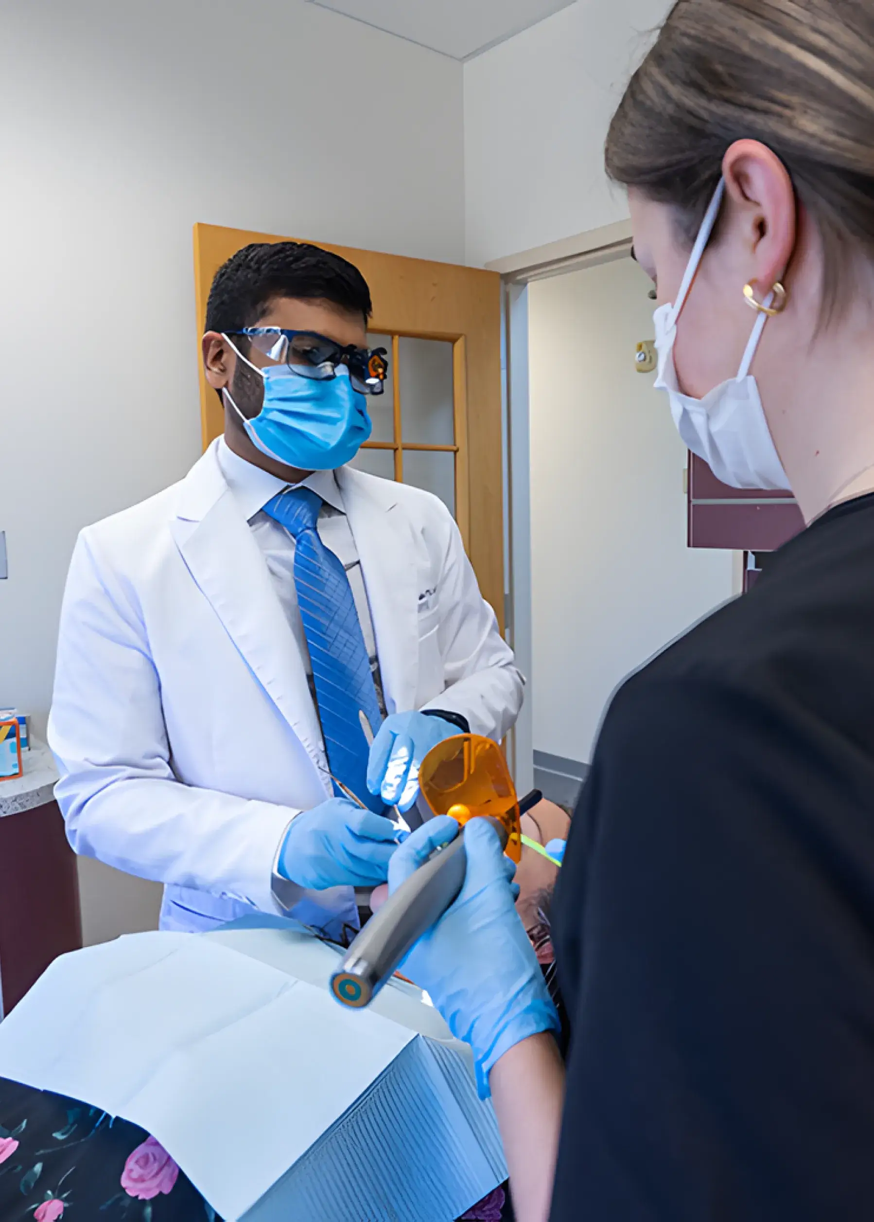 A dentist in a white coat and a dental assistant prepare tools for a procedure.
