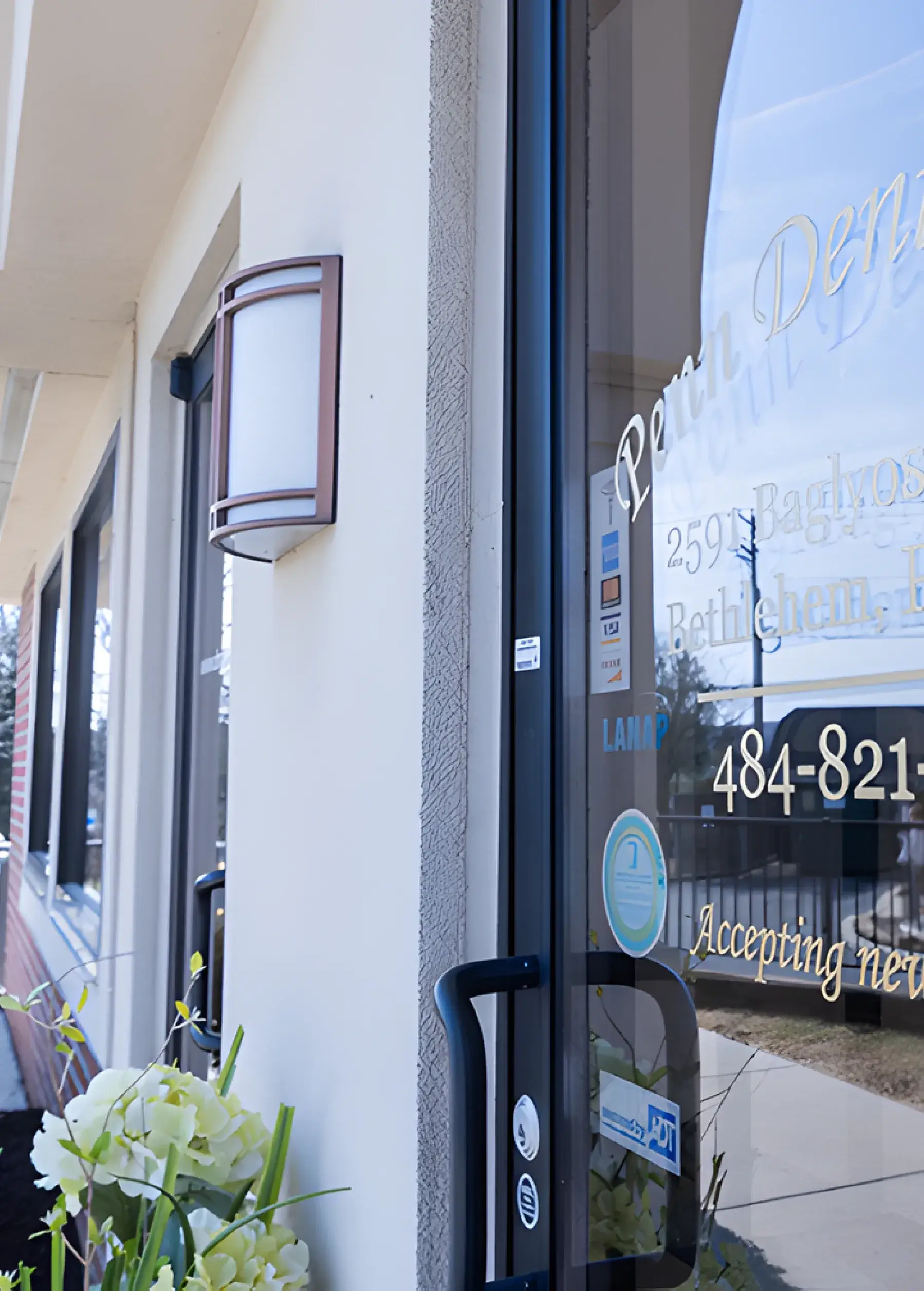 Entrance to a dental office with clear glass door and floral decoration outside.
