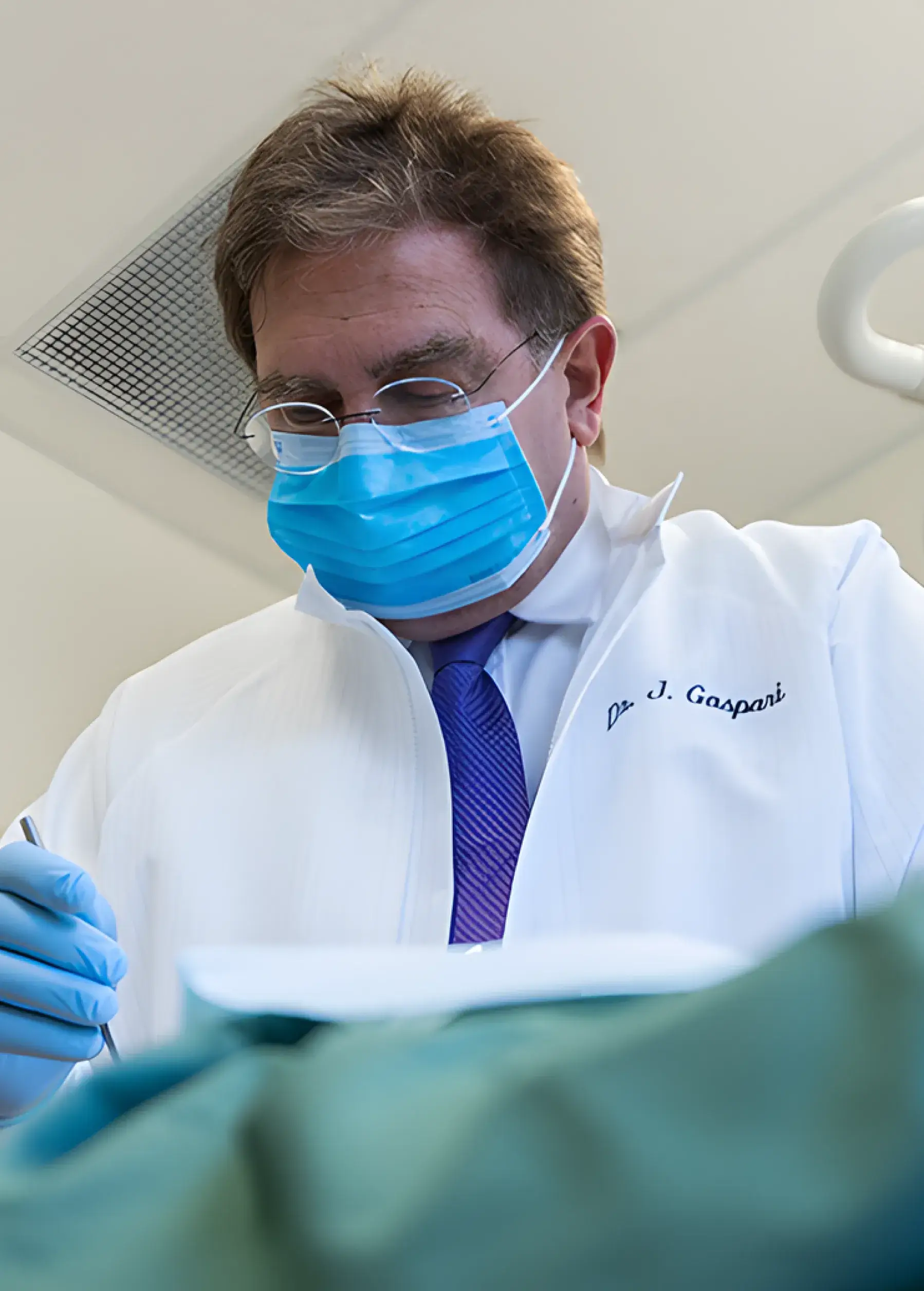 A dentist wearing a mask and gloves focuses on a dental procedure.