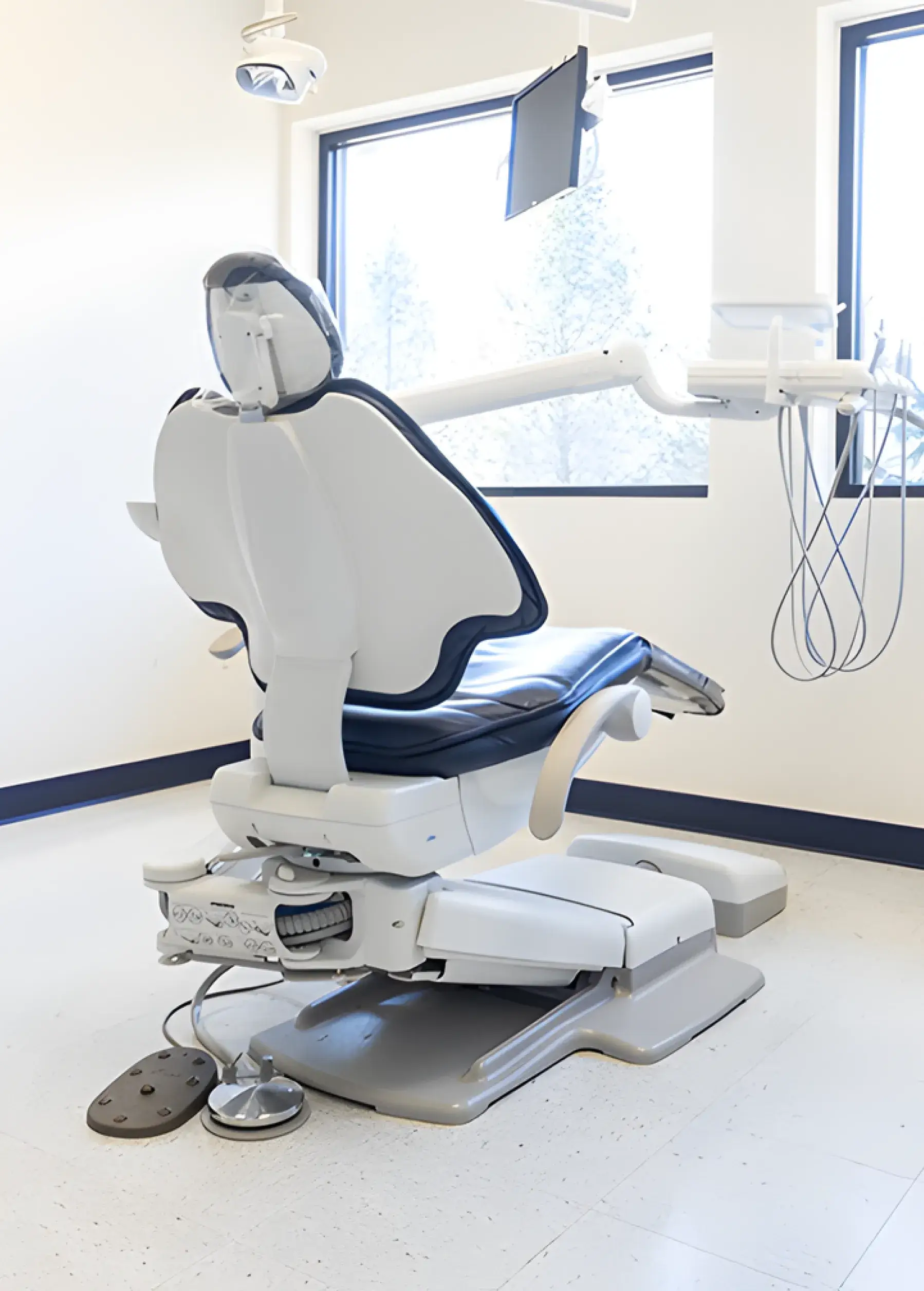 A dentist's chair in a clean, bright room with dental equipment attached.
