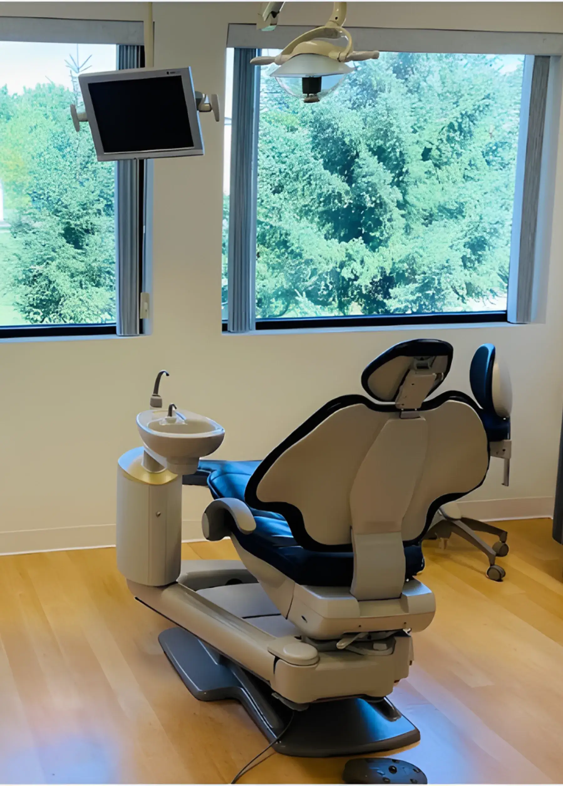 Dental chair in a bright room with a monitor and window view of trees.