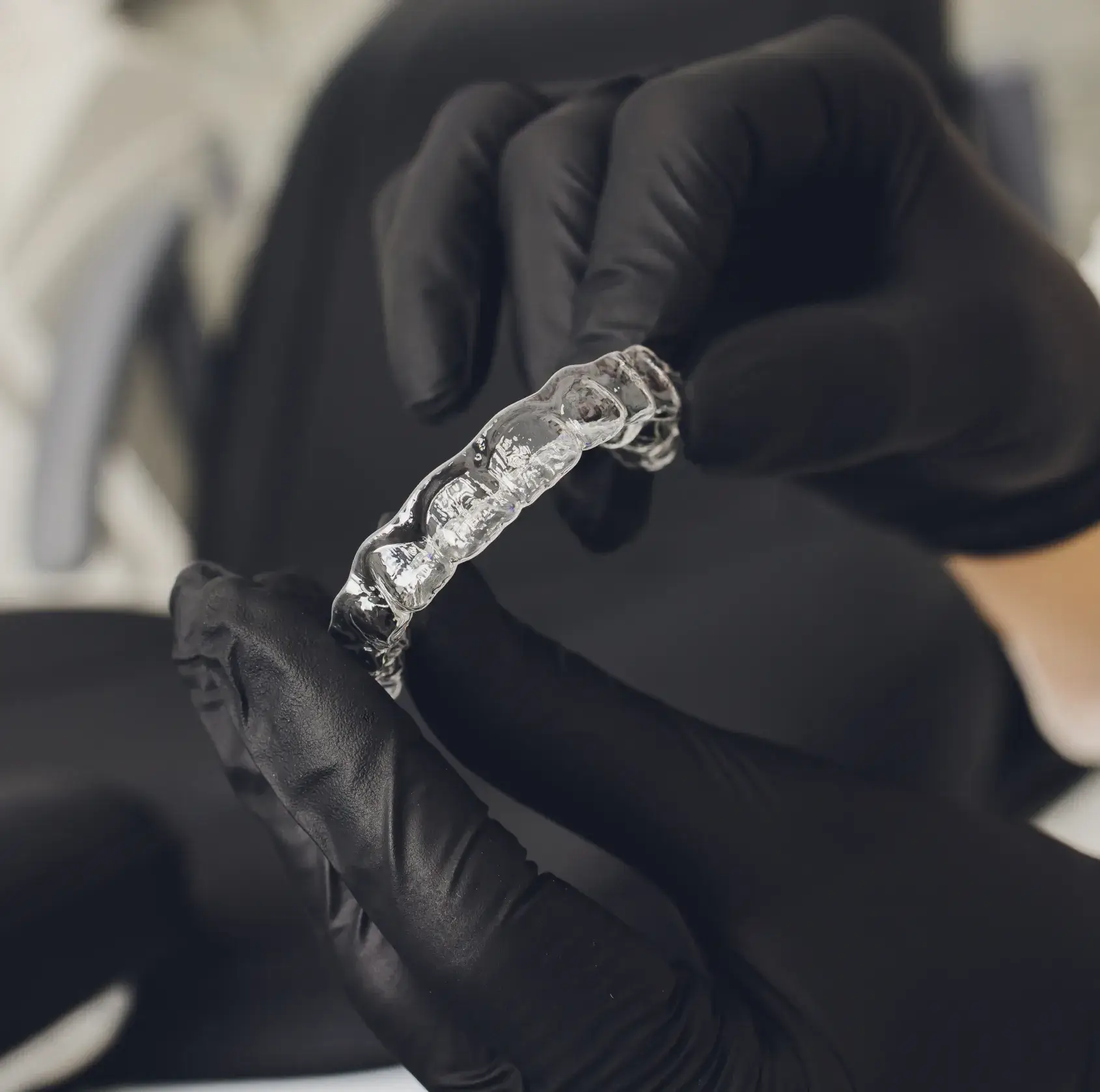 Person wearing black gloves holds a clear dental aligner with both hands.