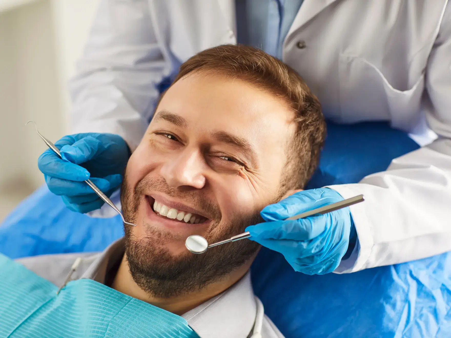 A man is smiling while a dentist examines his teeth with dental tools.