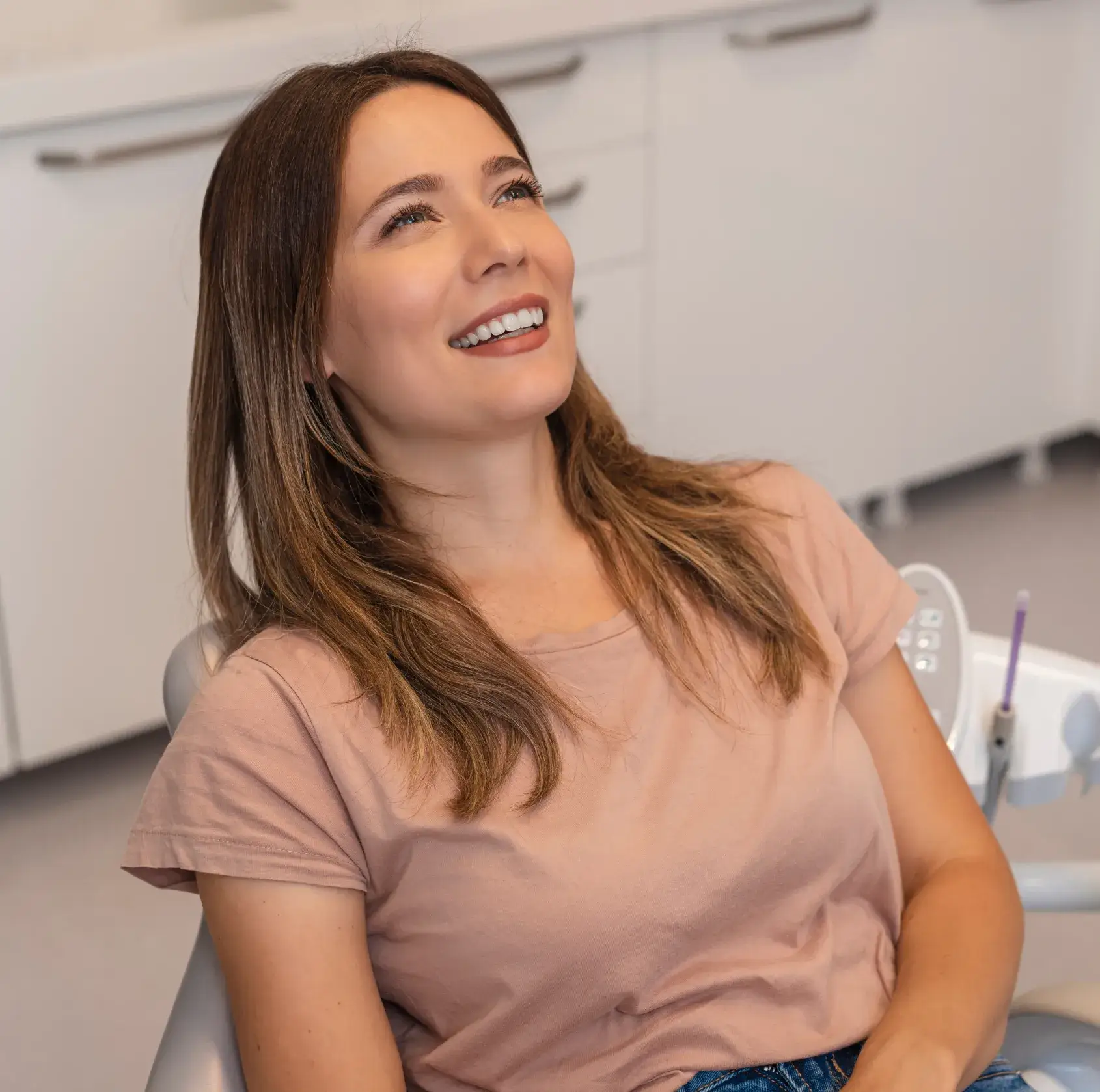 A woman in a dental chair smiles while looking upwards, appearing relaxed and happy.