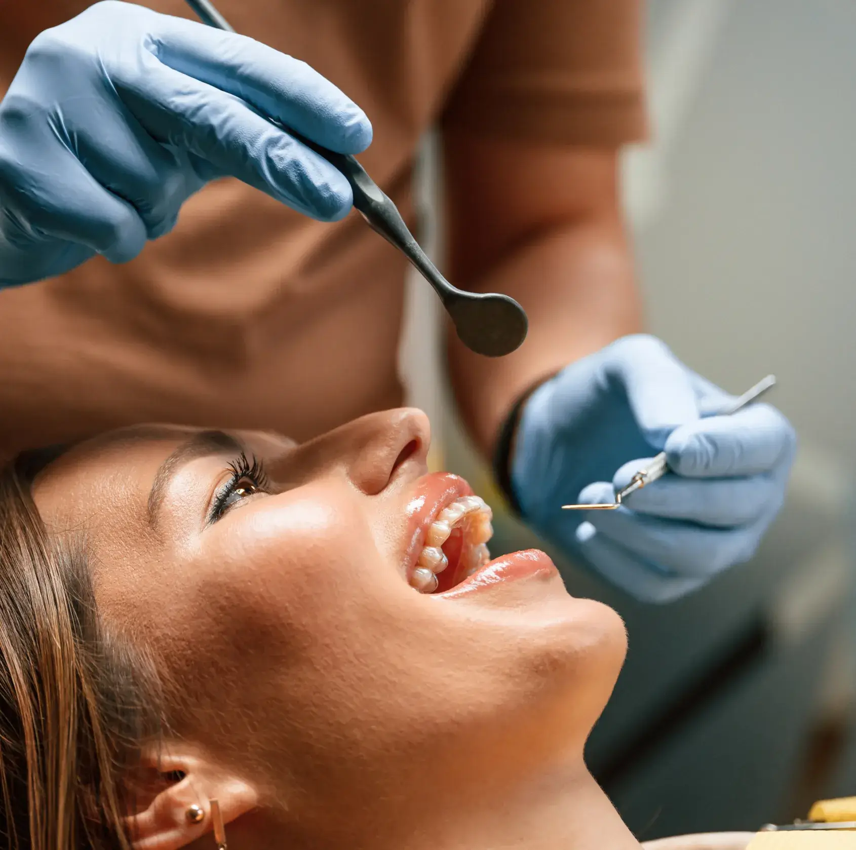 A dentist examines a patient's teeth using dental tools, while the patient lies in the chair.