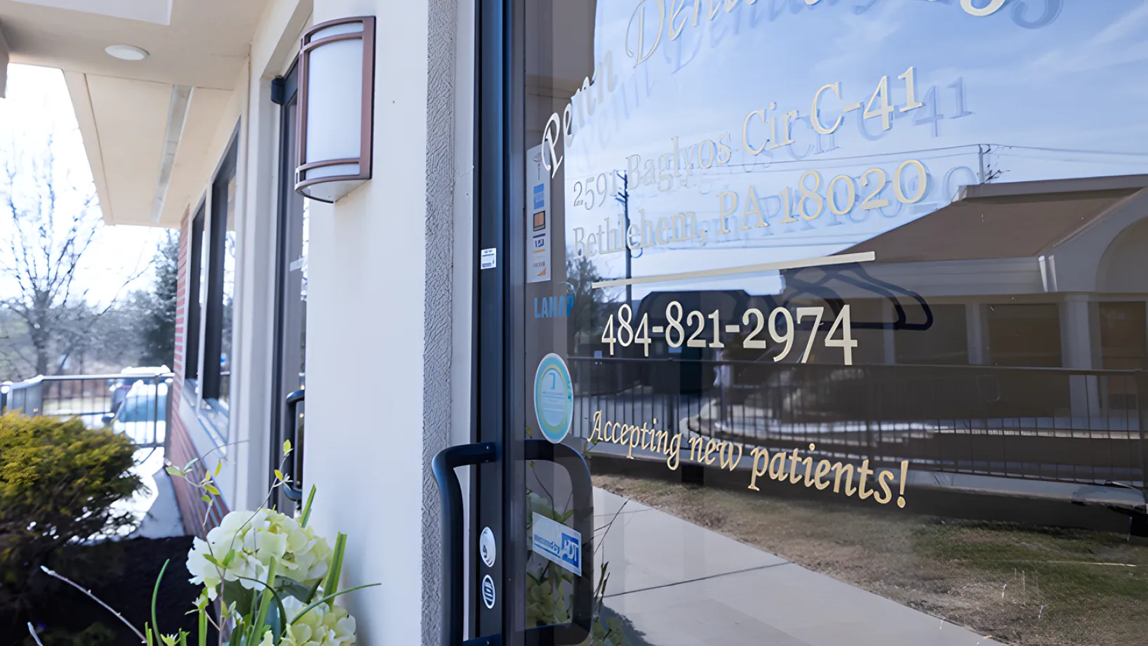 Glass door of a dental office with a sign saying, "Accepting new patients," and a phone number.