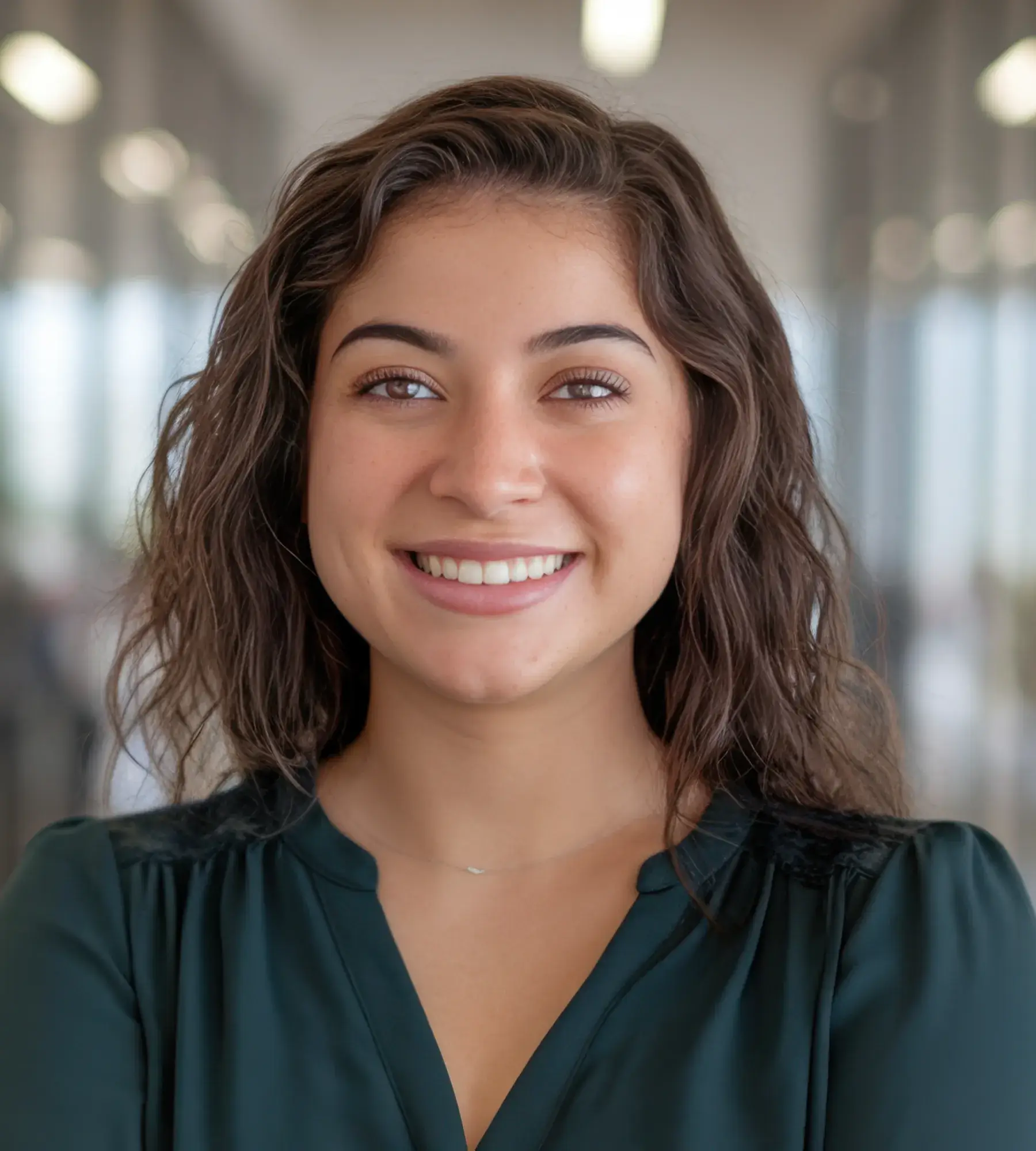 Young woman smiling indoors, wearing a dark green blouse.