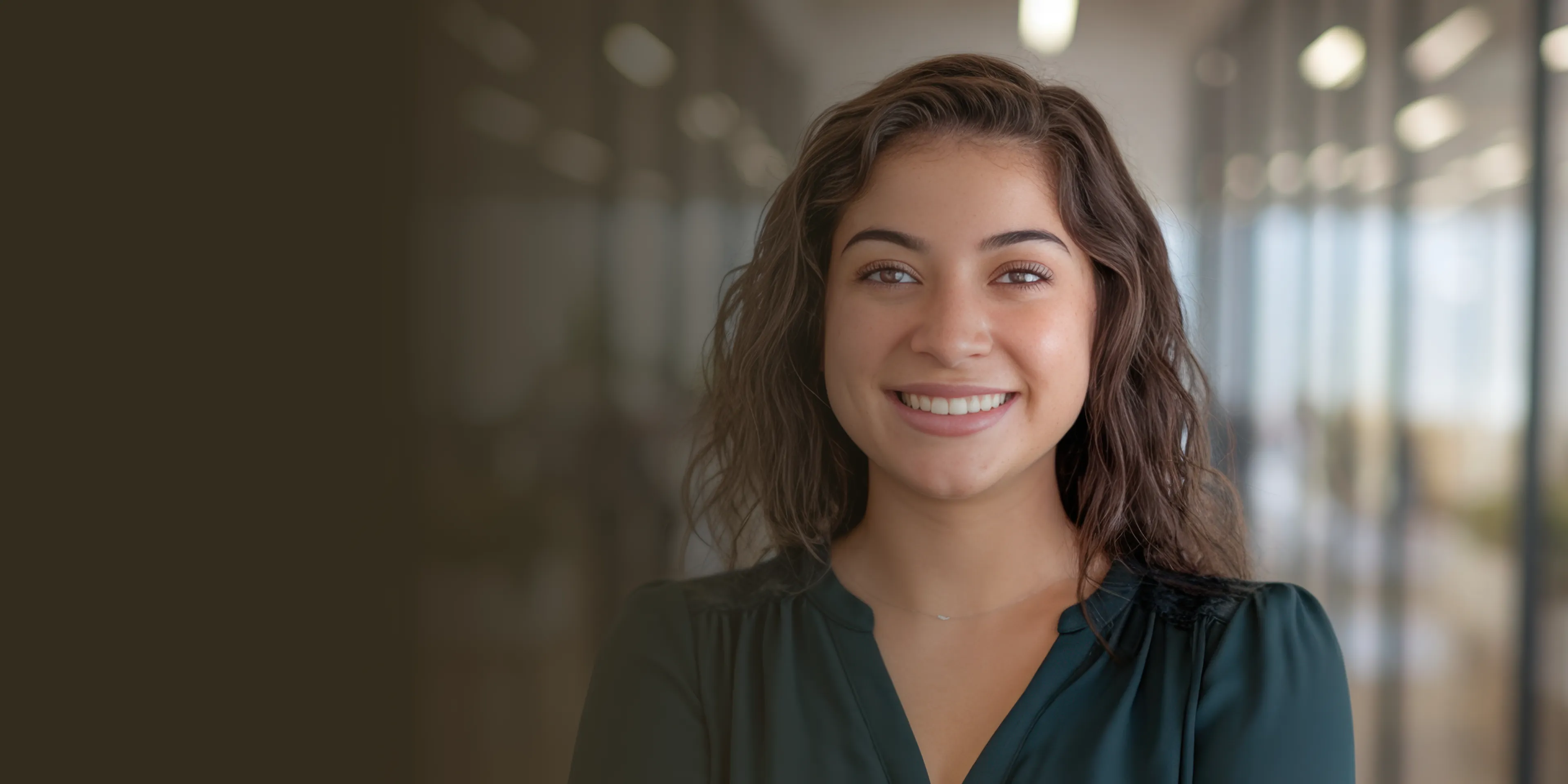 Smiling woman with curly hair stands in a hallway, looking directly at the camera.