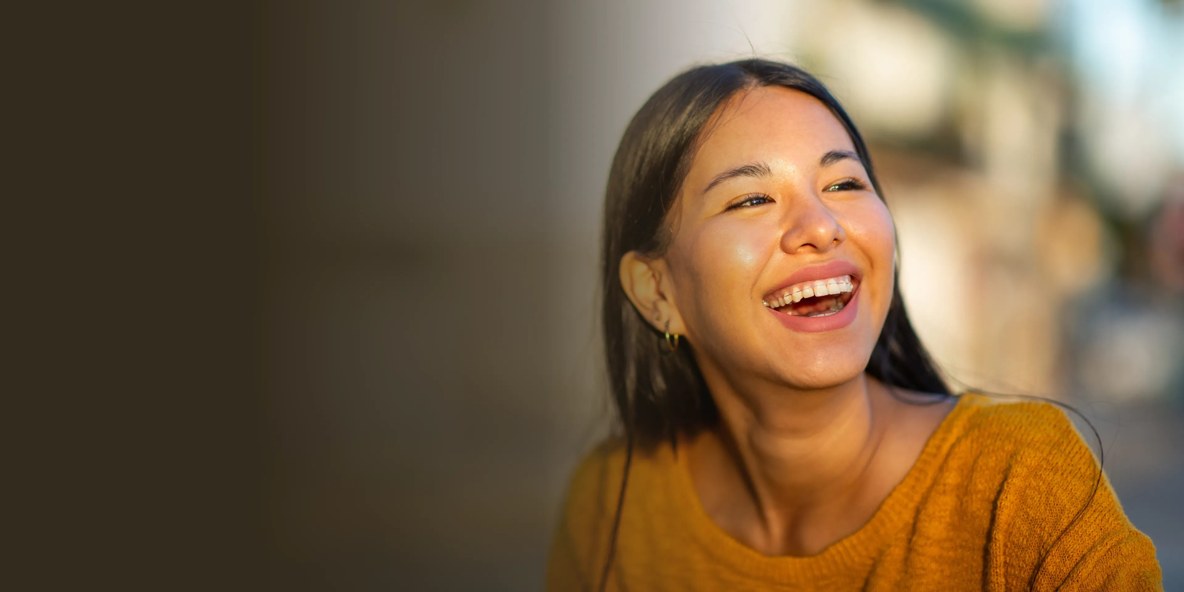 A woman in a yellow sweater is smiling and looking to the right.