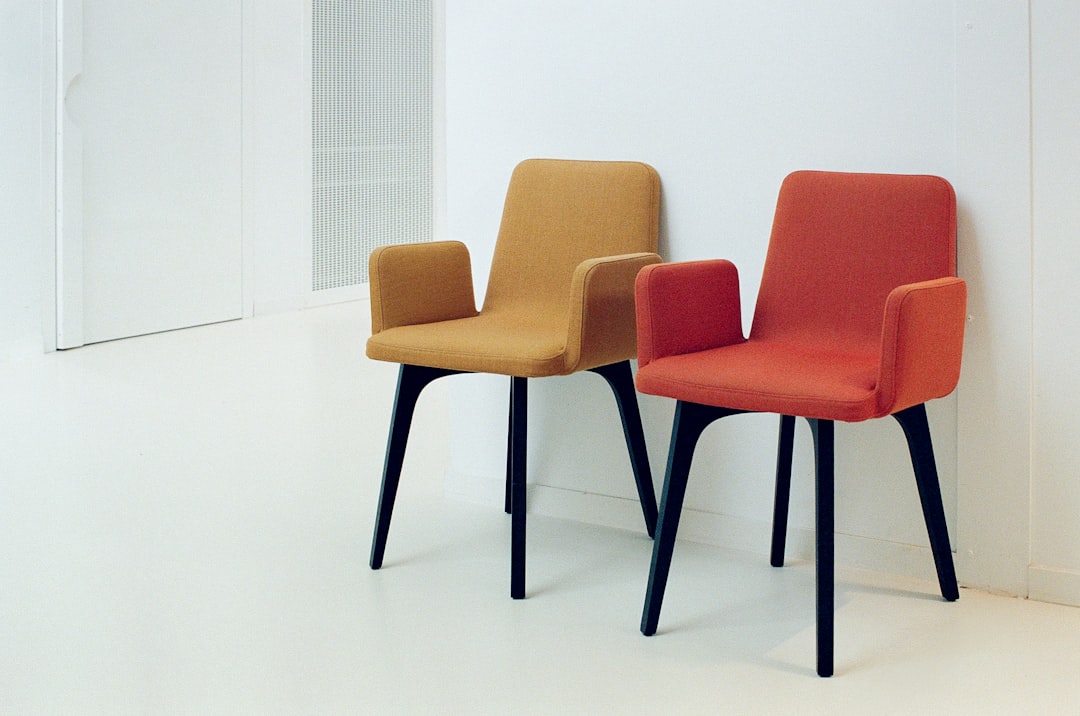 Two modern armchairs—one mustard yellow, the other coral red—against a clean white wall at the Musée Dobrée in Nantes, France. Photographed on Kodak Portra 400 with a Nikon F3 HP and 50mm lens.