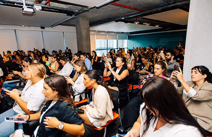 A full room of attendees, many taking photos or videos, during a dynamic indoor presentation.