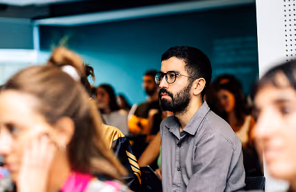 A man attentively listens during a presentation, surrounded by other engaged audience members.