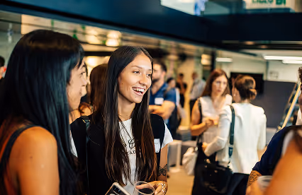 A group of attendees smiling and chatting during a networking session in a modern indoor venue.