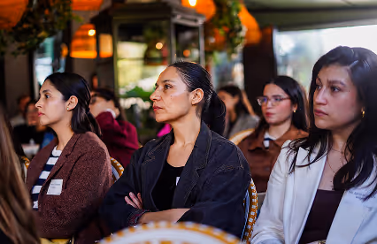 Close-up of audience members focused on a presentation, seated in rattan chairs under soft lighting.