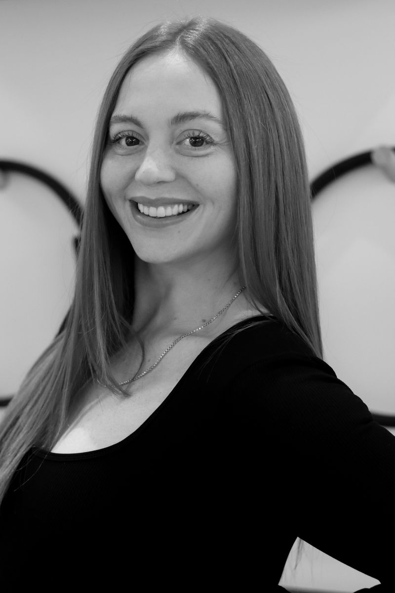 Smiling woman with long straight hair wearing a black top and a delicate chain necklace.