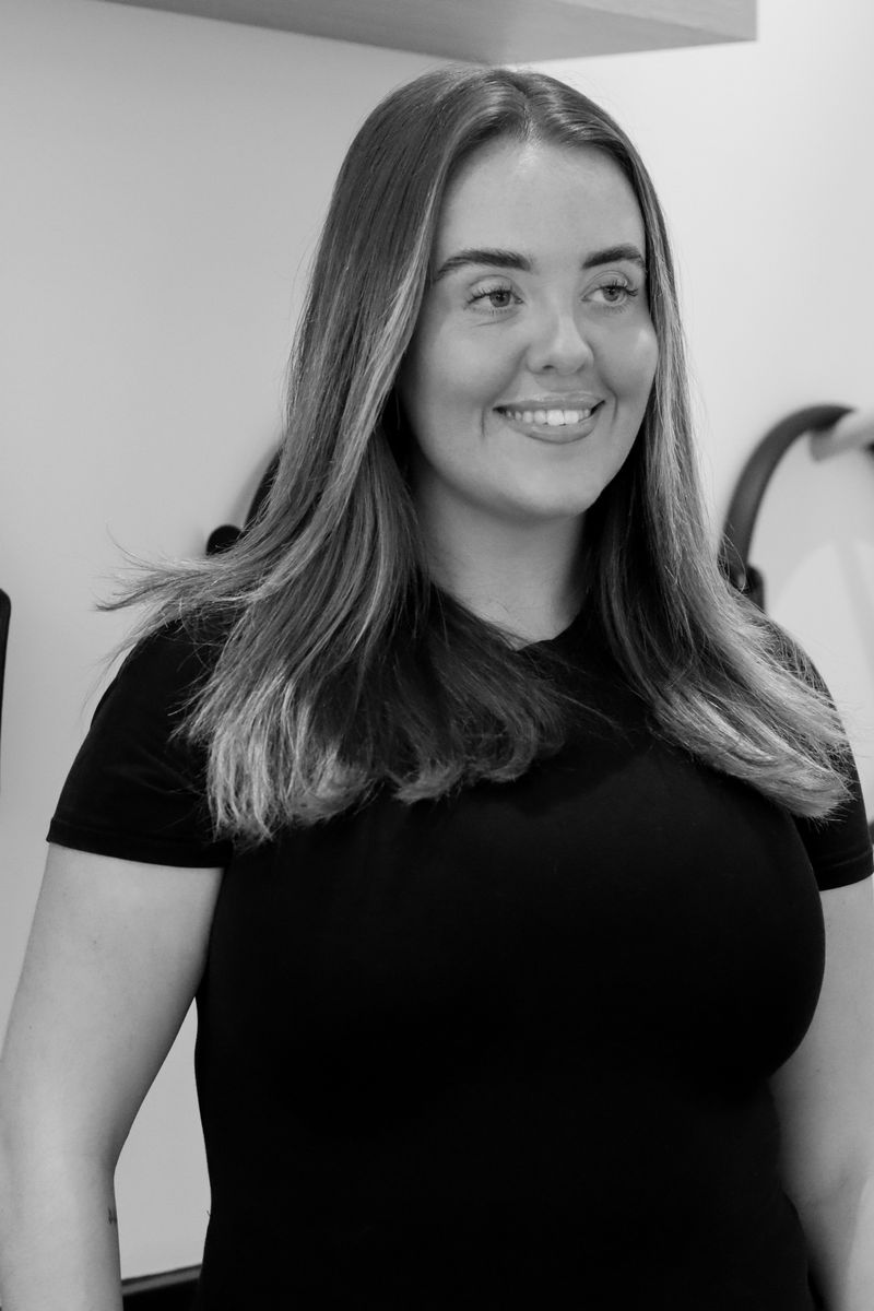 Smiling young woman with long straight hair wearing a black t-shirt, standing indoors.