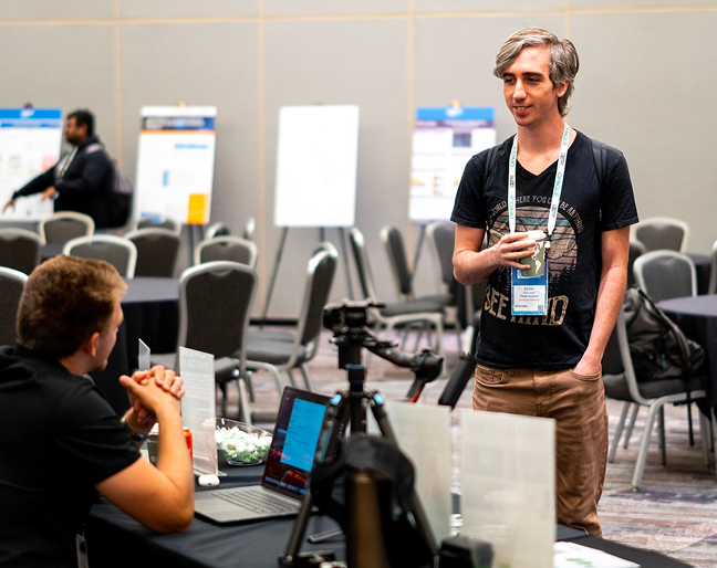 A person standing near a table and another seated person mid-conversation