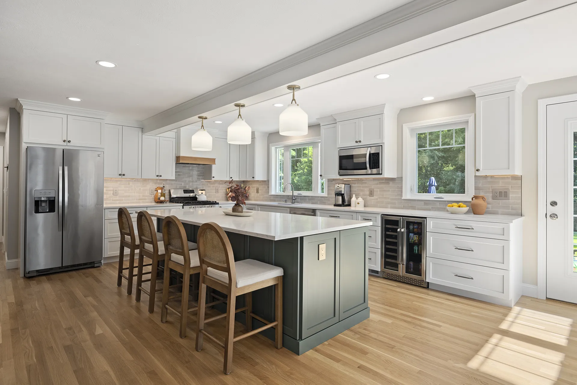 Bright renovated kitchen with green island, white cabinetry, pendant lights, and hardwood floors