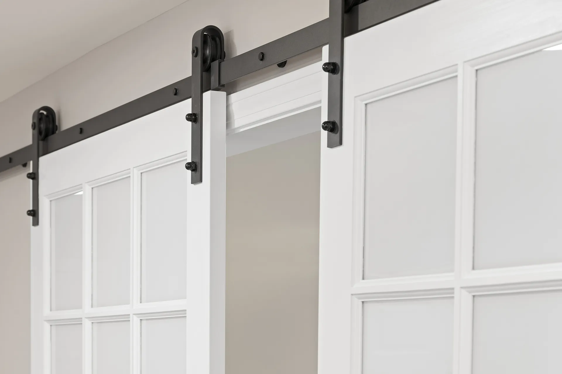 Close-up of black metal sliding barn door hardware on white French-style doors.