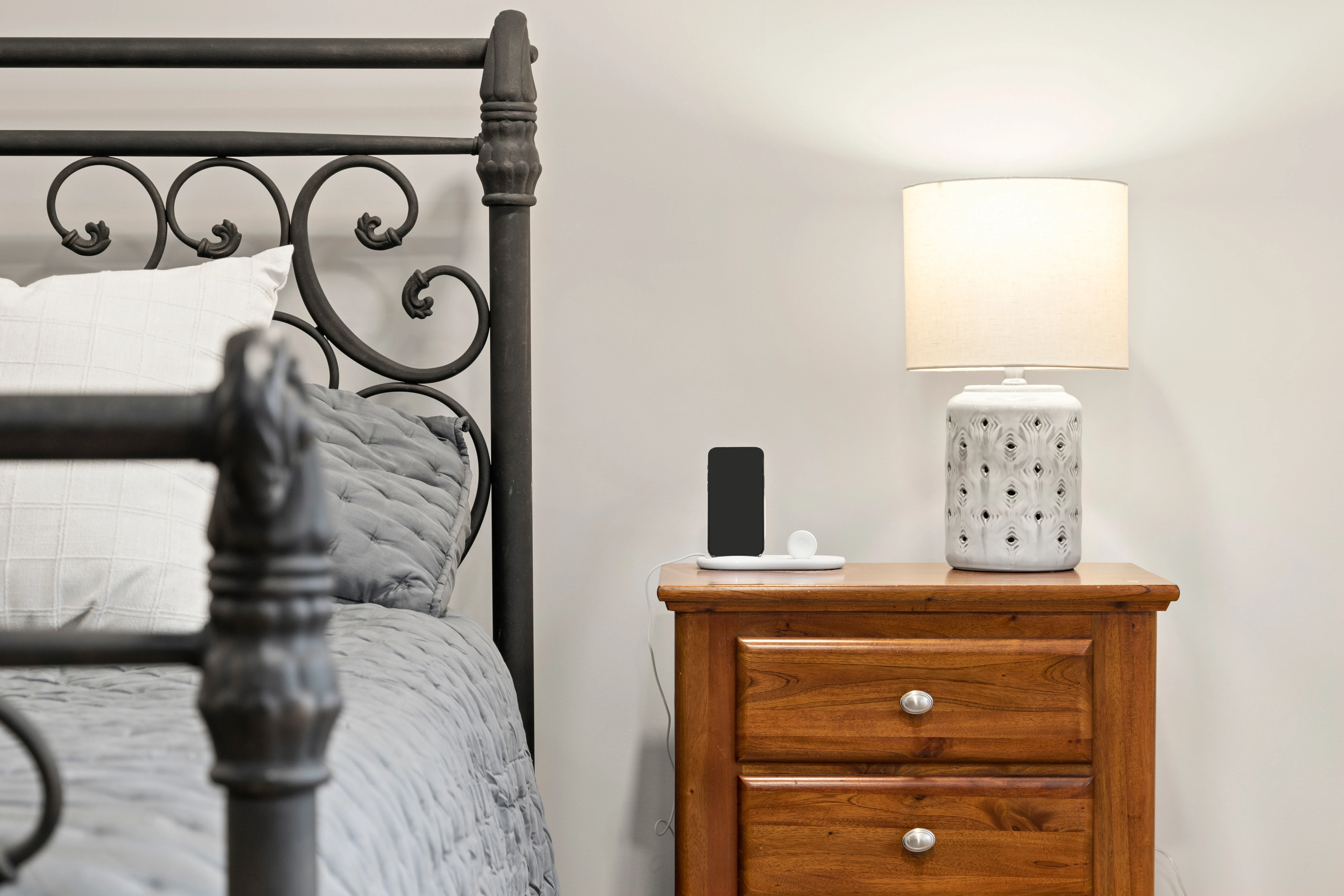 Bedside detail with wood nightstand, ceramic lamp, and wrought-iron bed frame.