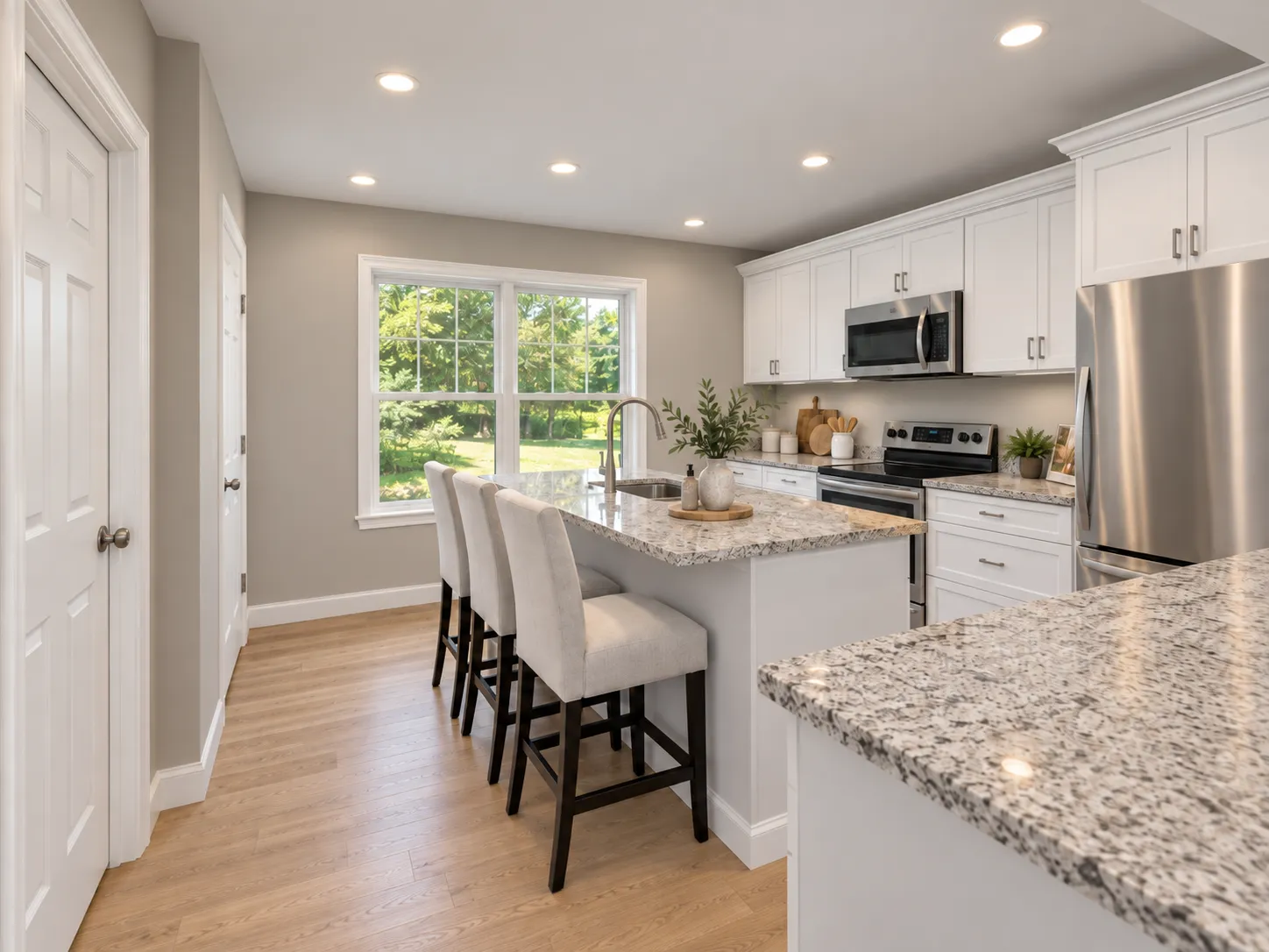 In-law suite kitchen in Pelham, NH — white shaker cabinetry, granite island with seating, open to the living room