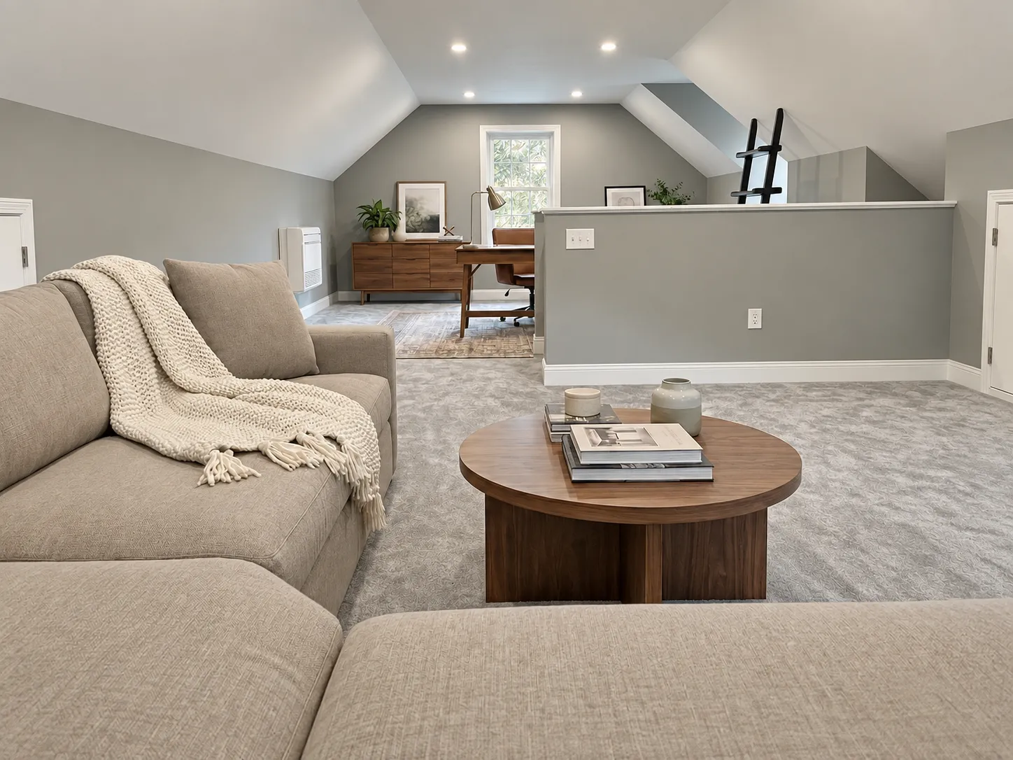 Attic remodel in Amherst, NH: finished attic lounge with a sectional and coffee table, home office nook with desk beyond, by Oak Hill Design & Build