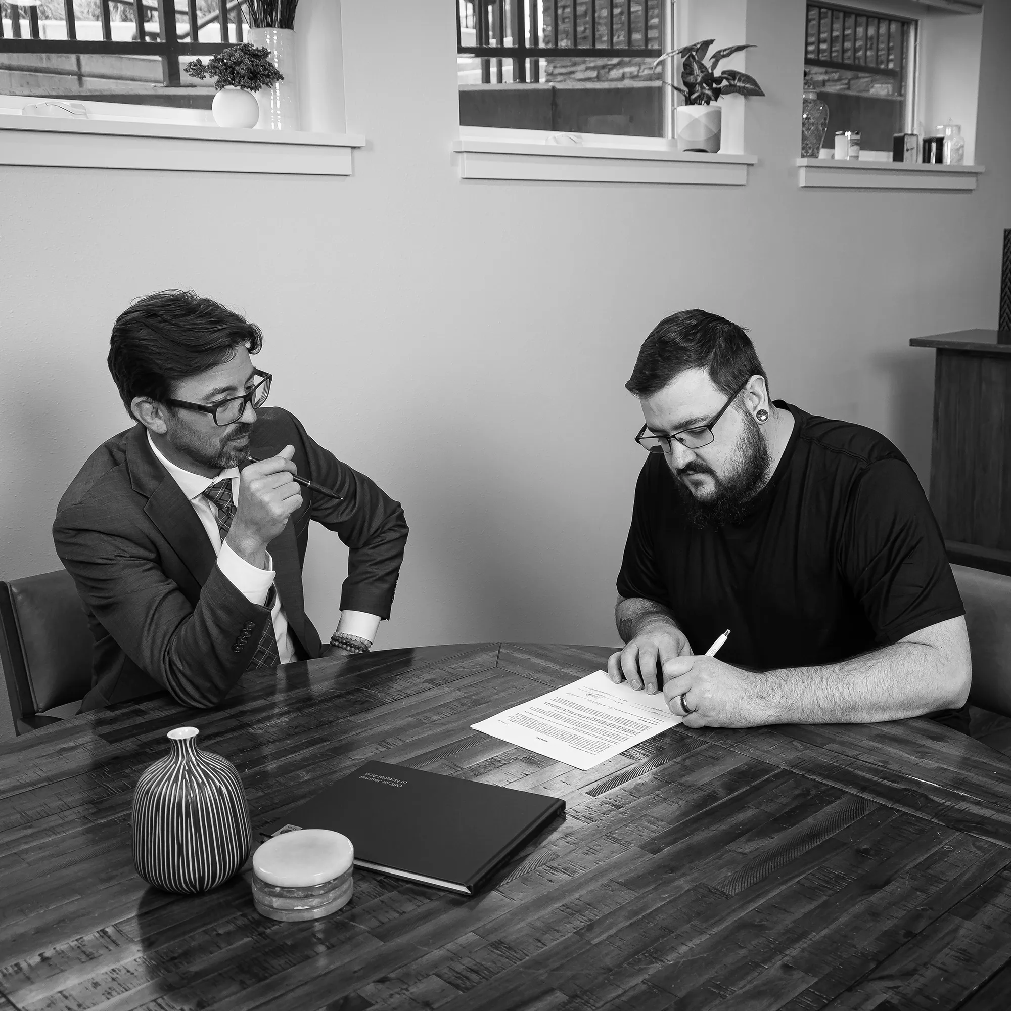 Keith watches thoughtfully as a client signs a document at a table.