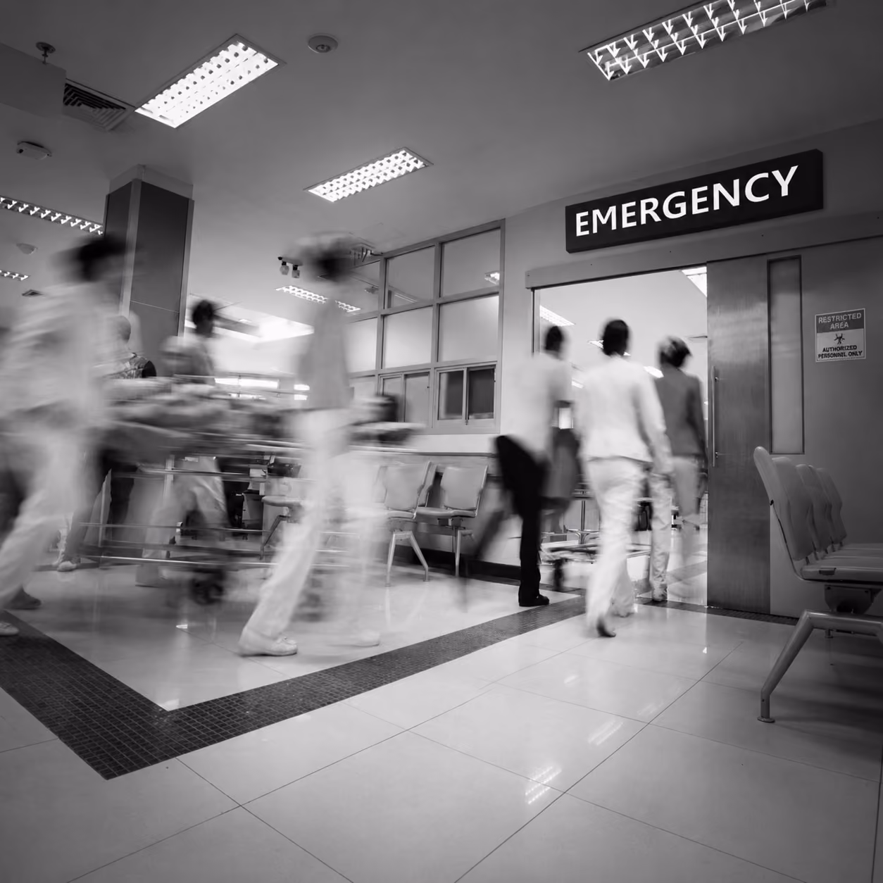 A black-and-white motion blurred photograph of a patient on stretcher being pushed at speed through a hospital corridor.