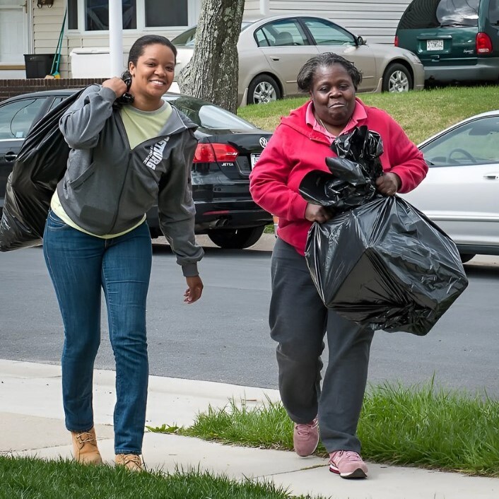 Two women walking in the sidewalk carrying a bag.