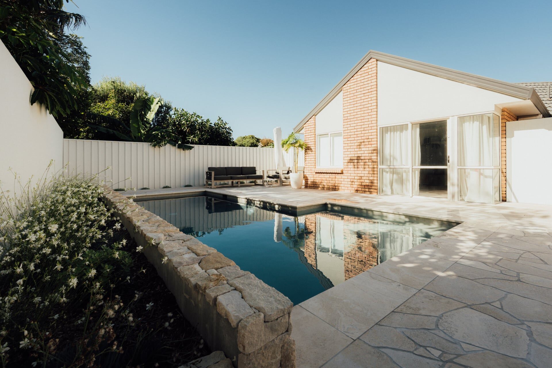 Modern house exterior with curved stone retaining wall landscaped gardens and timber features at Marine Parade project
