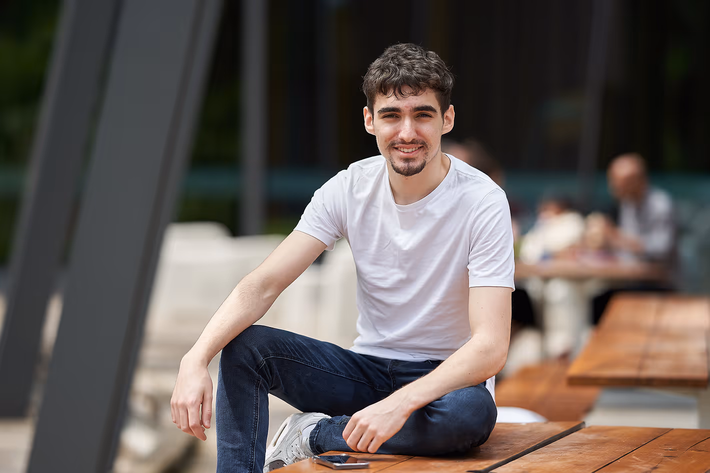 Photo of a young guy sitting outside on a bench smiling at the camera