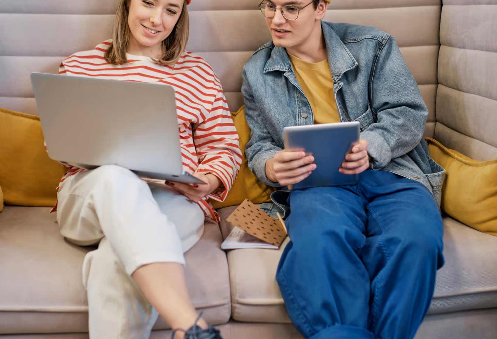 Two young people sitting on a couch looking at a lap top