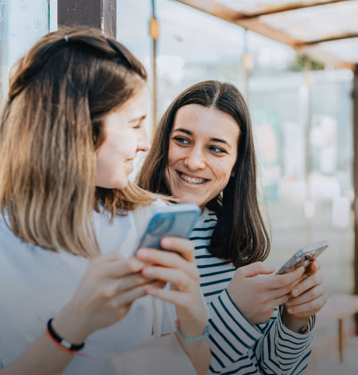 Photo of two young girls on their phones and smiling at each other