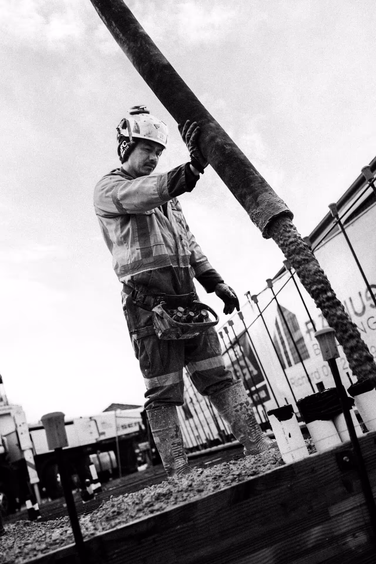 Construction worker in safety gear guiding pouring concrete at a building site.