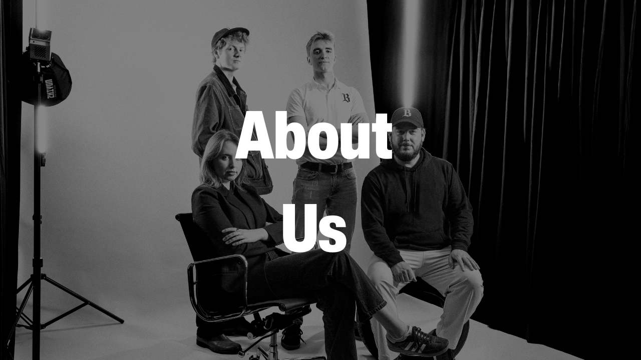 Black and white photo of four people posing in a studio with the text 'About Us' overlaid.