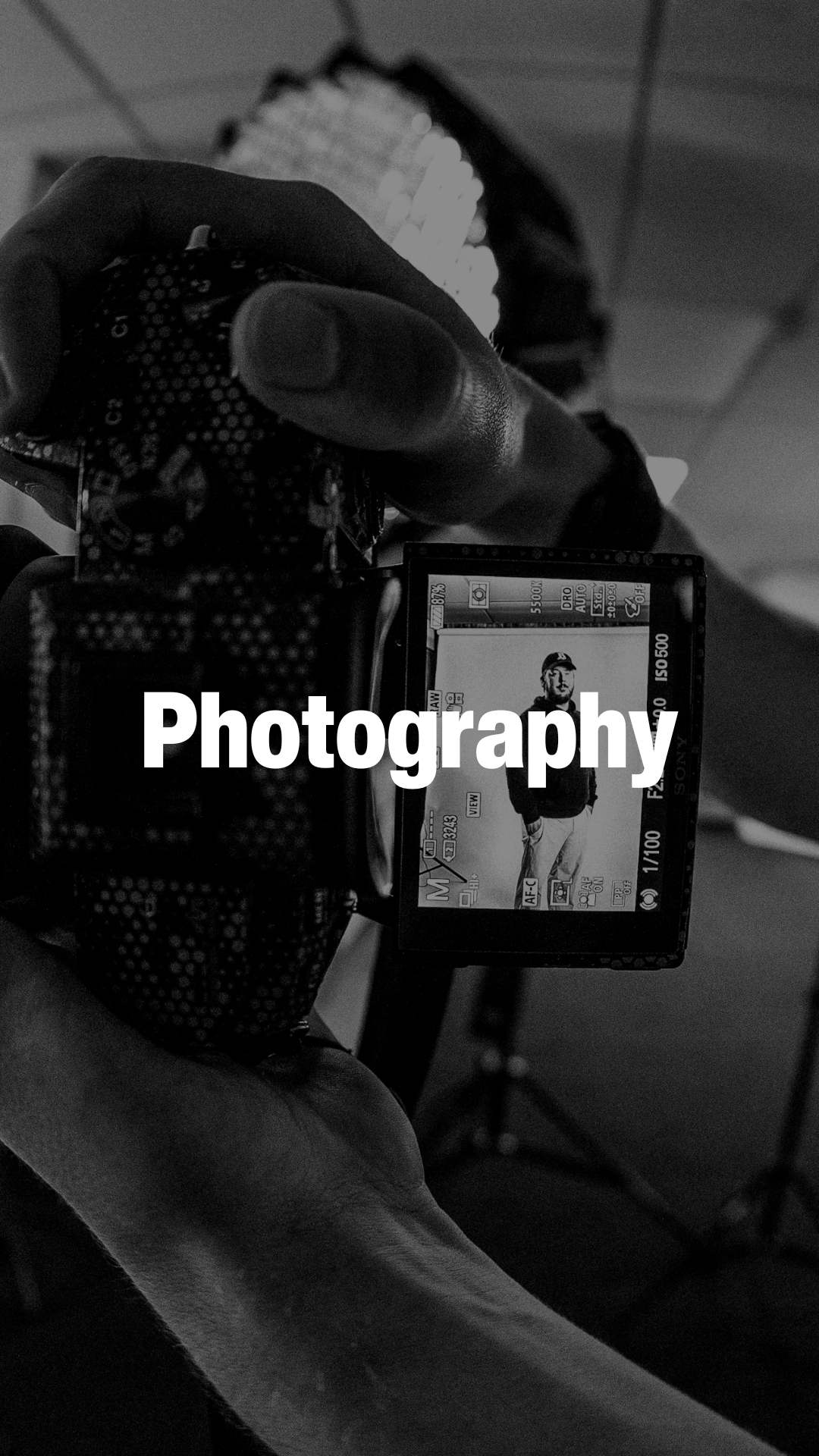 Close-up of a person holding a camera showing a man wearing a cap and casual clothes on the camera screen, with the word 'Photography' overlaid.