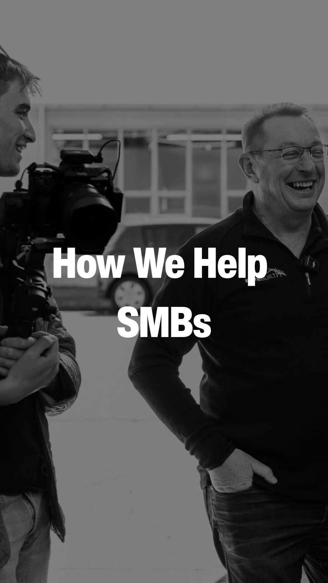 Two men smiling and talking, one holding a video camera, with the text 'How We Help SMBs' overlayed.