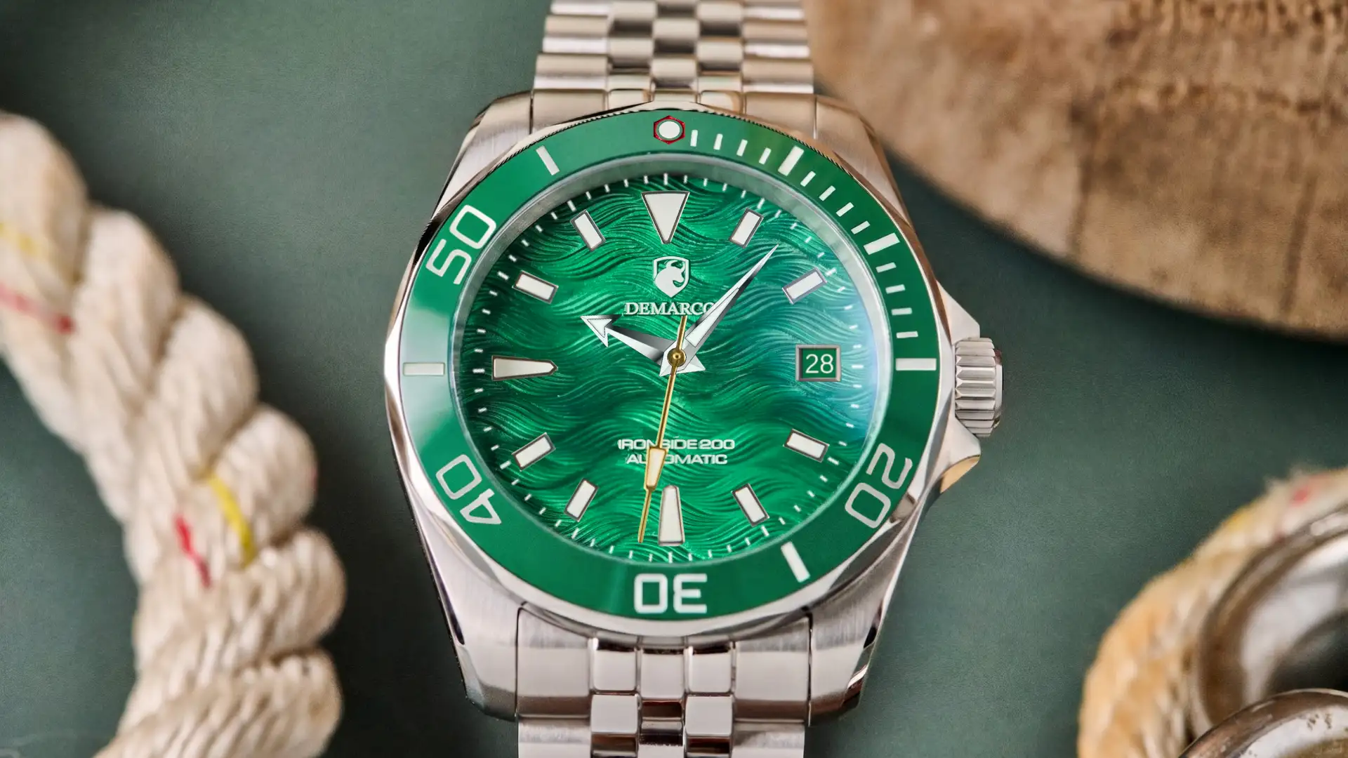 The DeMarco Ironside 200 with a green dial on a steel jubilee bracelet, resting on a green surface beside marine rope